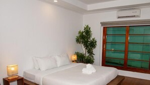 A neatly made bed with white linens and a rolled towel, a small bedside table with a lamp, a potted plant, and a window with a view. - Casa Mezcaleria (Boracay Island)
