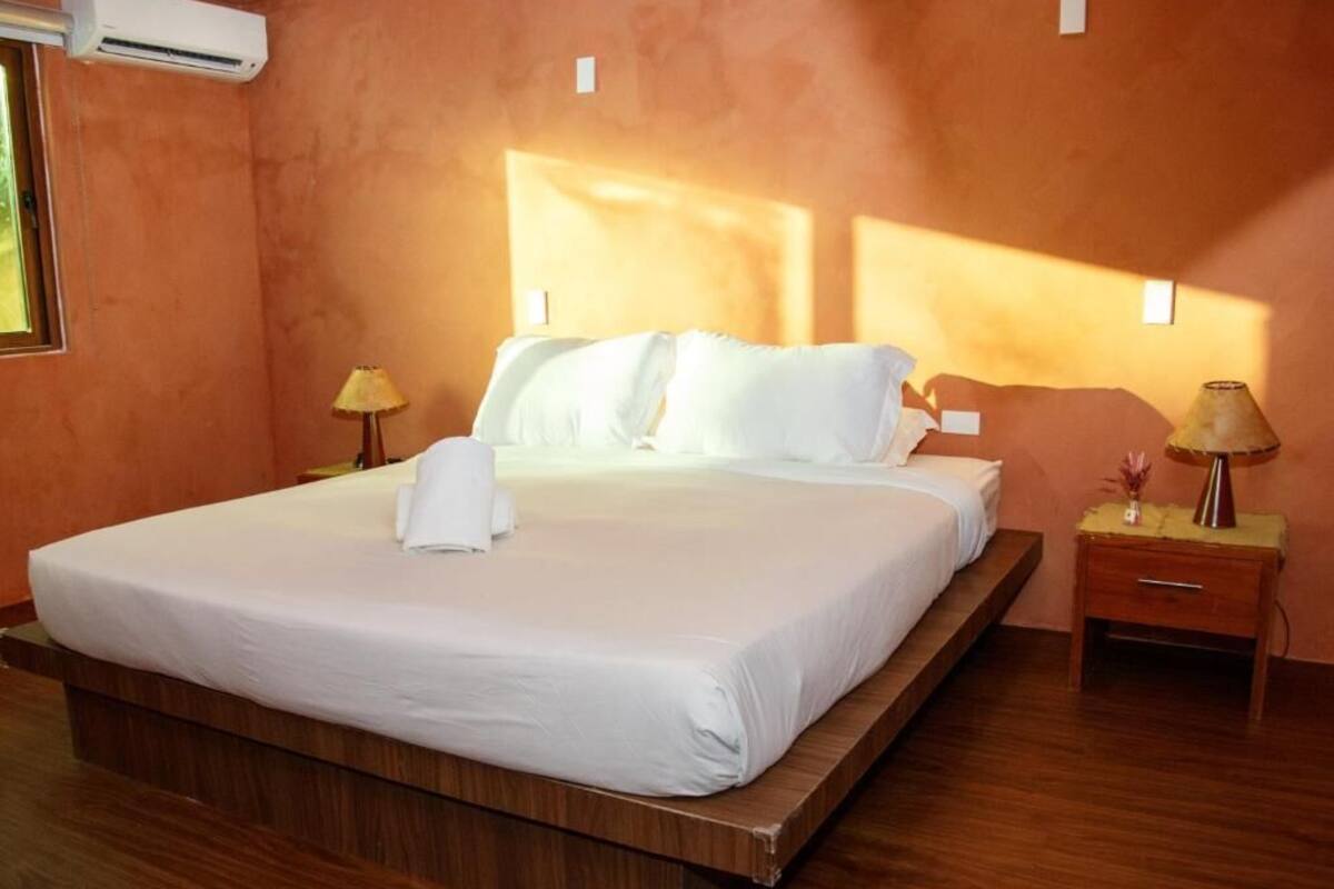 Une chambre d’hôtel avec un grand lit, un plancher en bois, deux lampes de chevet et un appareil de climatisation.