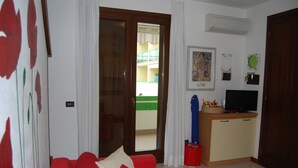 Una sala de estar con un sofá rojo, un televisor sobre un mueble de madera y un ventanal corredizo que da a un balcón.