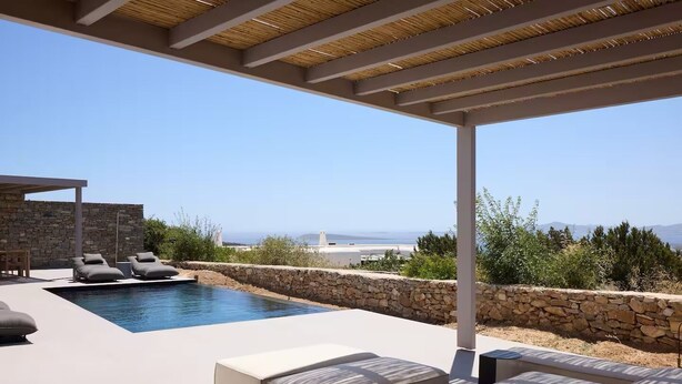 A modern outdoor pool area with stone walls, lounge chairs, and a pergola. - Villa Mae by ΜΡS (Agkeria)