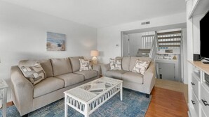 Un salon avec un canapé beige, une table basse blanche et un tapis bleu.