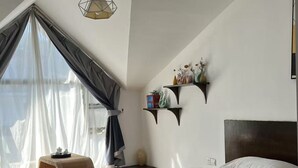 A modern bedroom with a large bed, a window with sheer curtains, a hanging light fixture, and a small shelf with decorative items. - Zhangjiajie YunYe Hotel (Zhangjiajie)