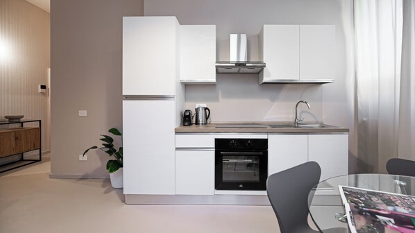 A modern kitchen with white cabinetry, a built-in oven, a coffee maker, and a glass dining table with chairs. - Giulini 5 (Monza)