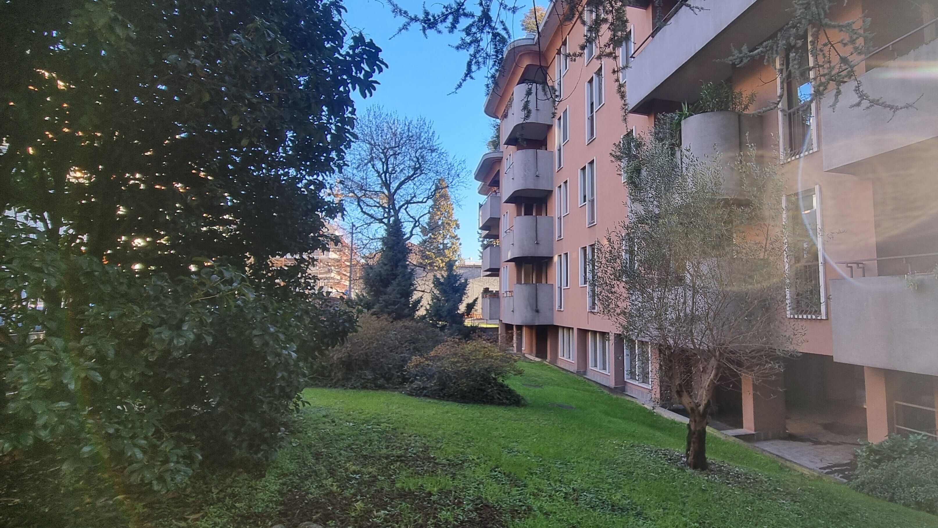 A residential building with multiple balconies, a well-maintained lawn, and surrounding trees.