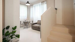 Una sala de estar moderna con un sofá, una mesa de comedor y sillas. Se ve una escalera que conduce a otro nivel.