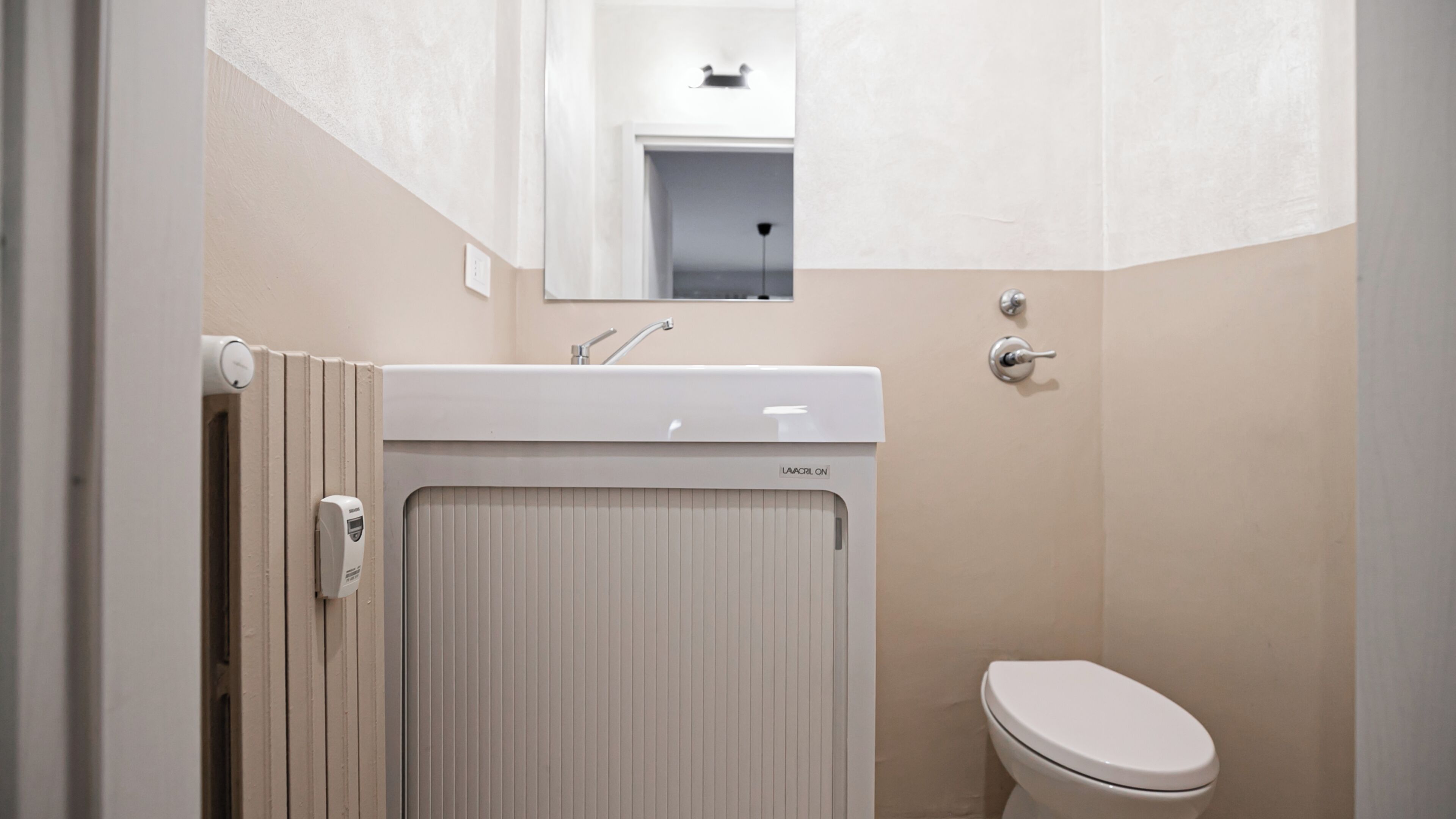 Une salle de bain avec des toilettes blanches, un lavabo avec un robinet et un miroir au-dessus du lavabo.