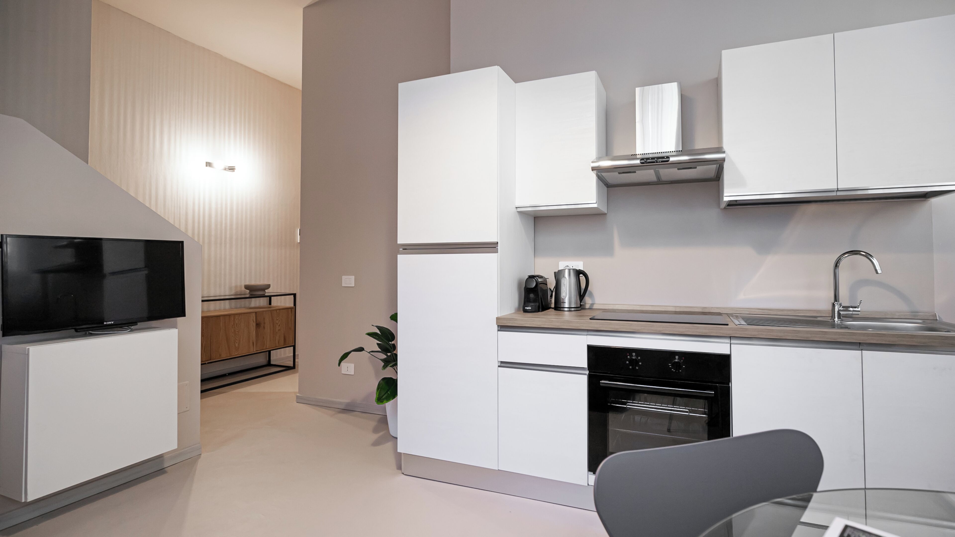 A modern kitchen with white cabinetry, a built-in oven, a coffee maker, and a sink with a faucet.