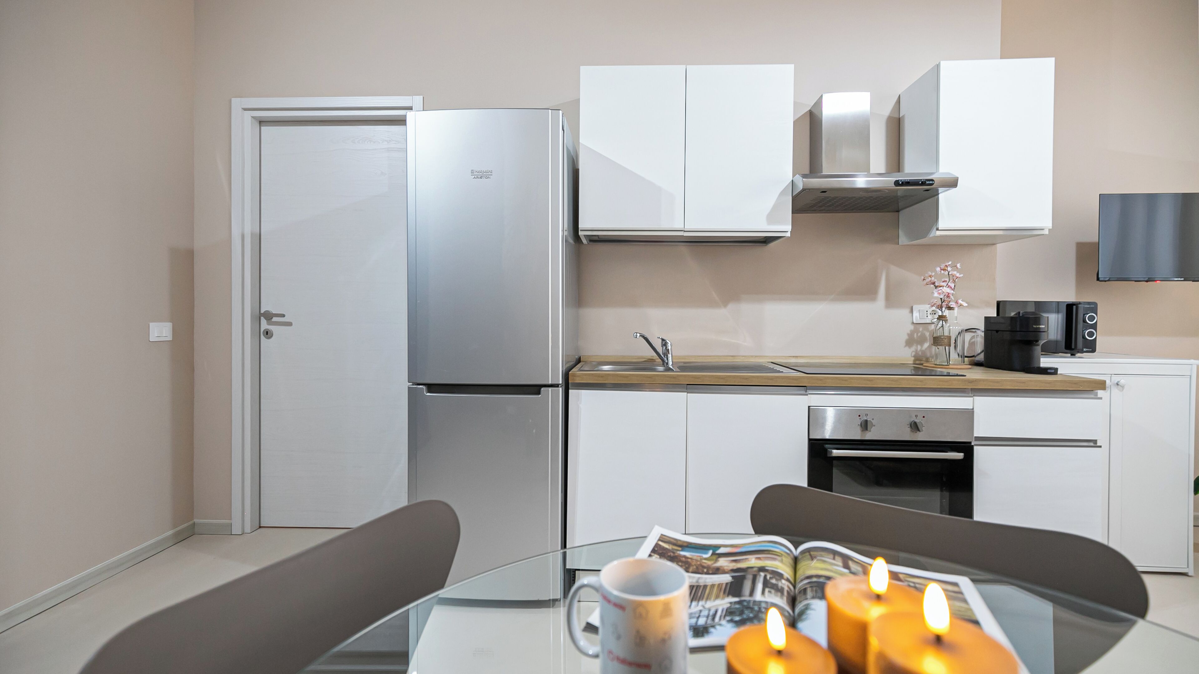 A modern kitchen with a refrigerator, oven, and microwave. There is a dining table with a magazine and candles.