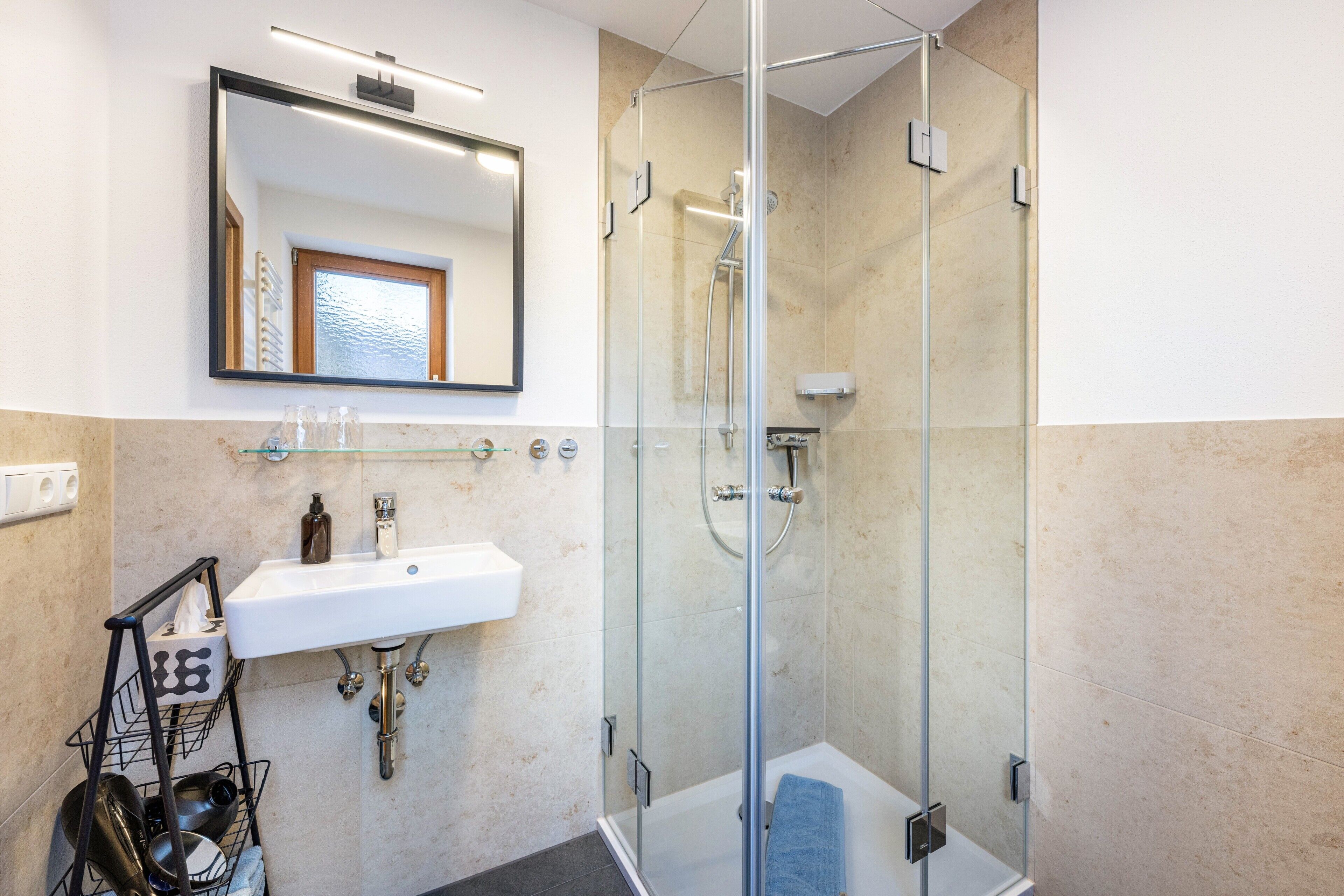 A modern bathroom with a glass-enclosed shower, a white sink, and a mirror above it.