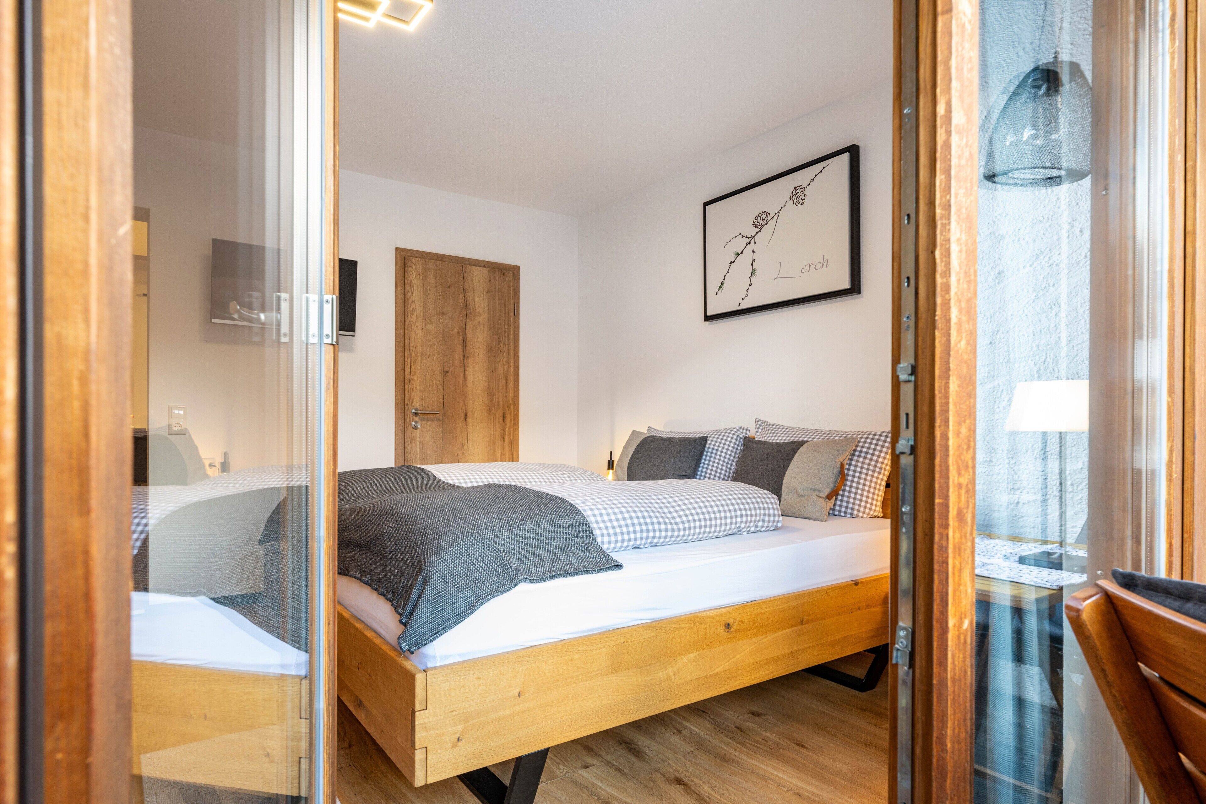 Une chambre à coucher avec un lit en bois, un téléviseur fixé au mur et une œuvre d’art encadrée.