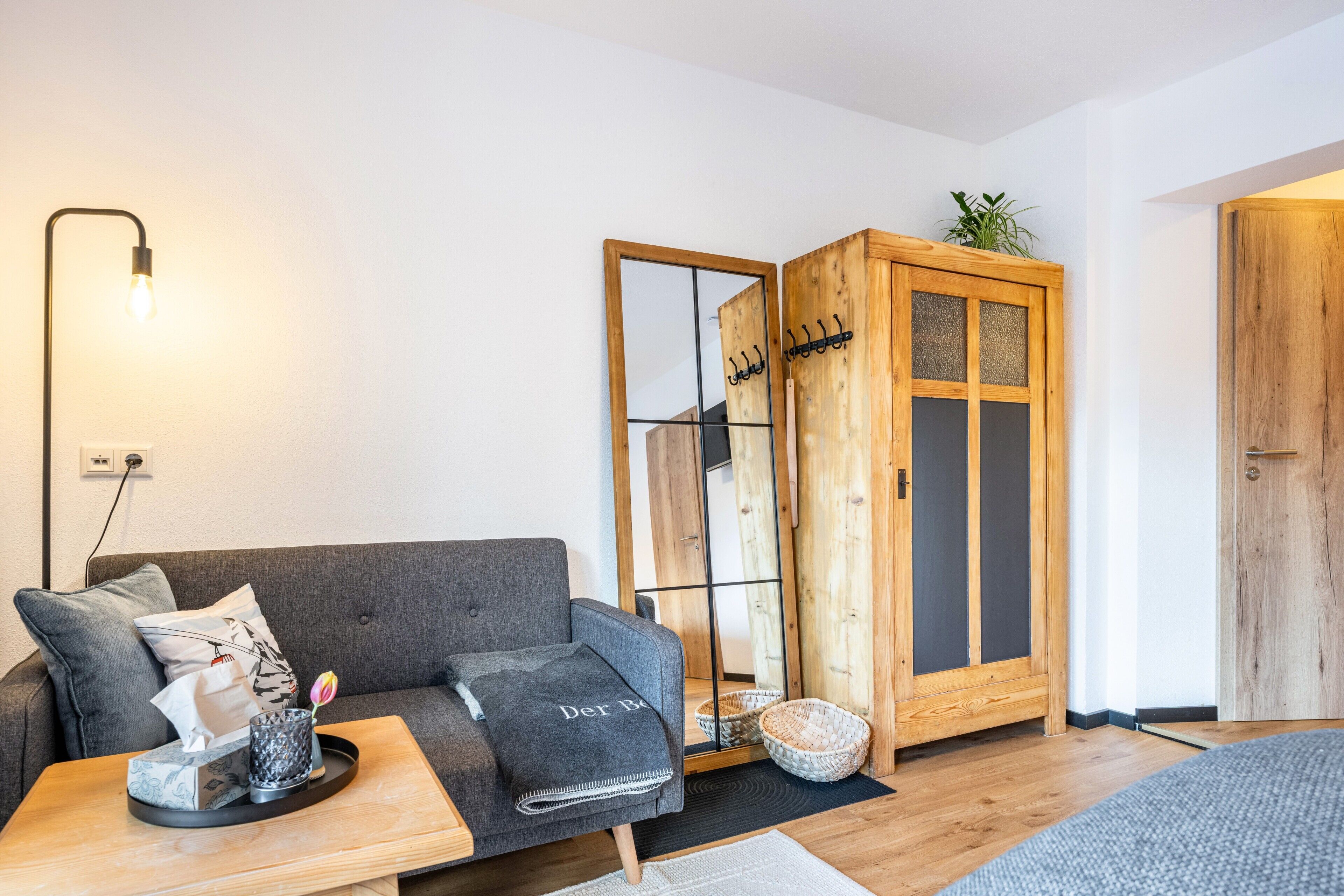 A modern living room with a grey sofa, a wooden cabinet, a small table with a tray, and a wall-mounted lamp.