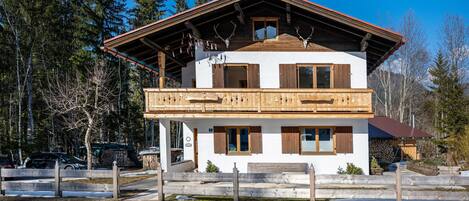 A two-story chalet with a balcony, wooden shutters, and a stone foundation.