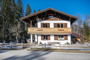 En tvåvånings chalet med en balkong, träpersienner och en grund av sten.
