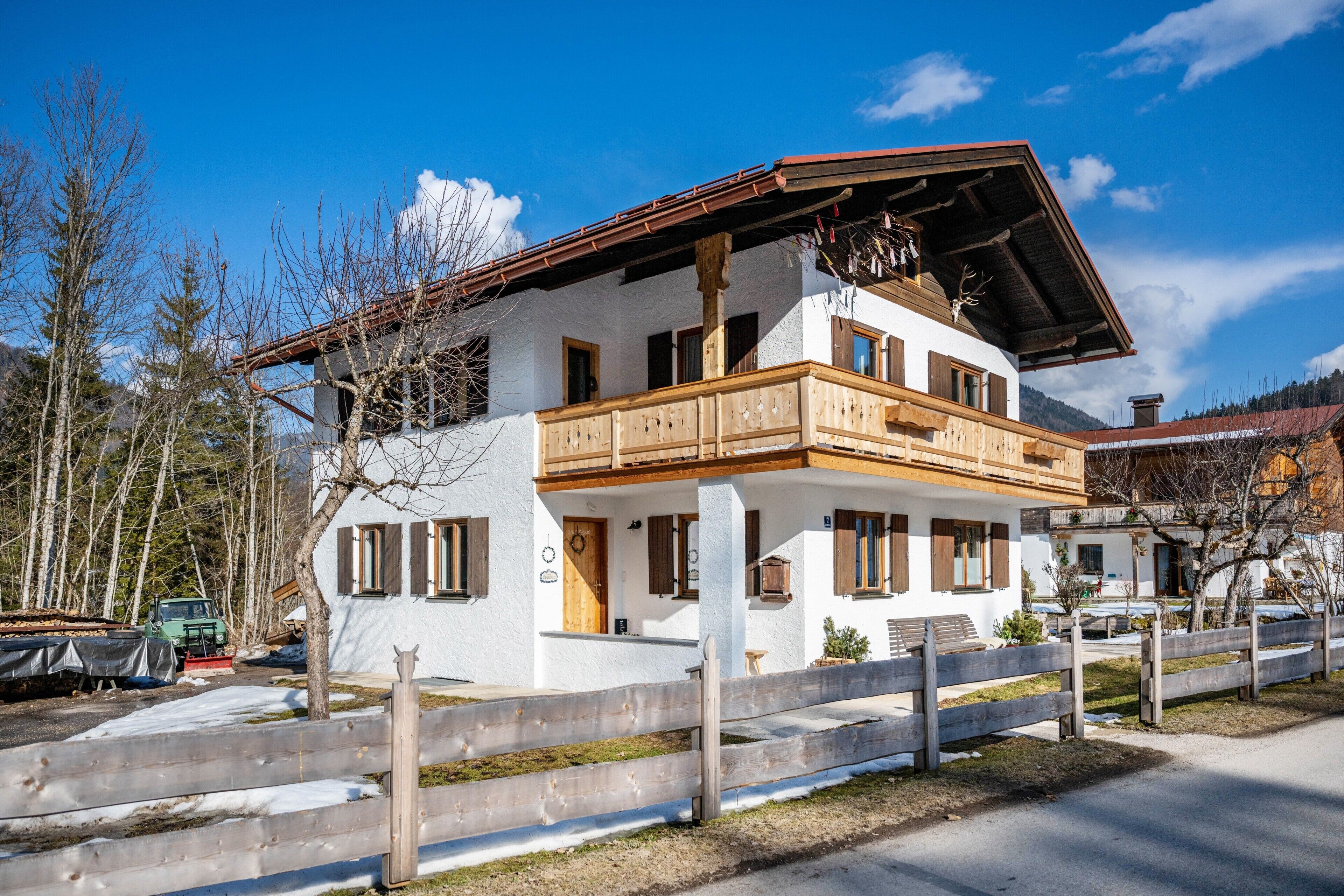 Un chalet de dos pisos con balcón, vigas de madera y montañas al fondo.