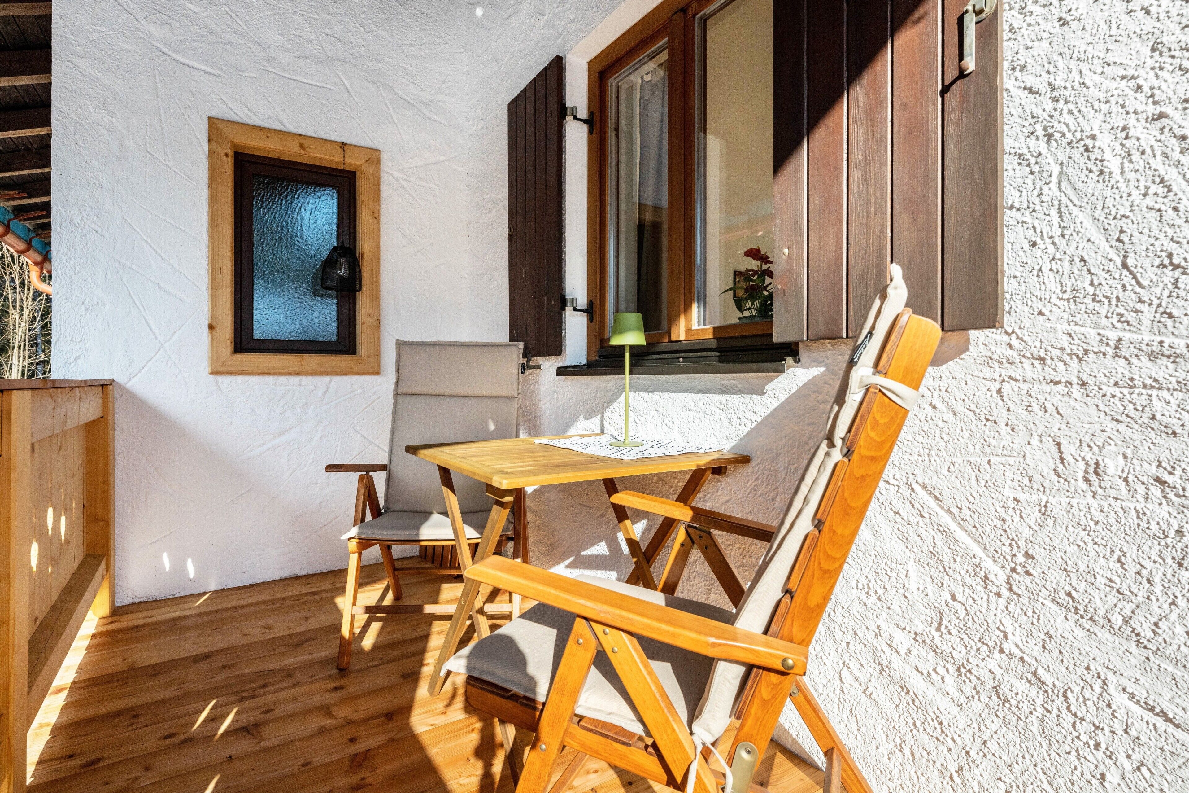 Eine Holzterrasse mit Tisch und Stühlen, ein Fenster mit Rollläden und einer Lampe.