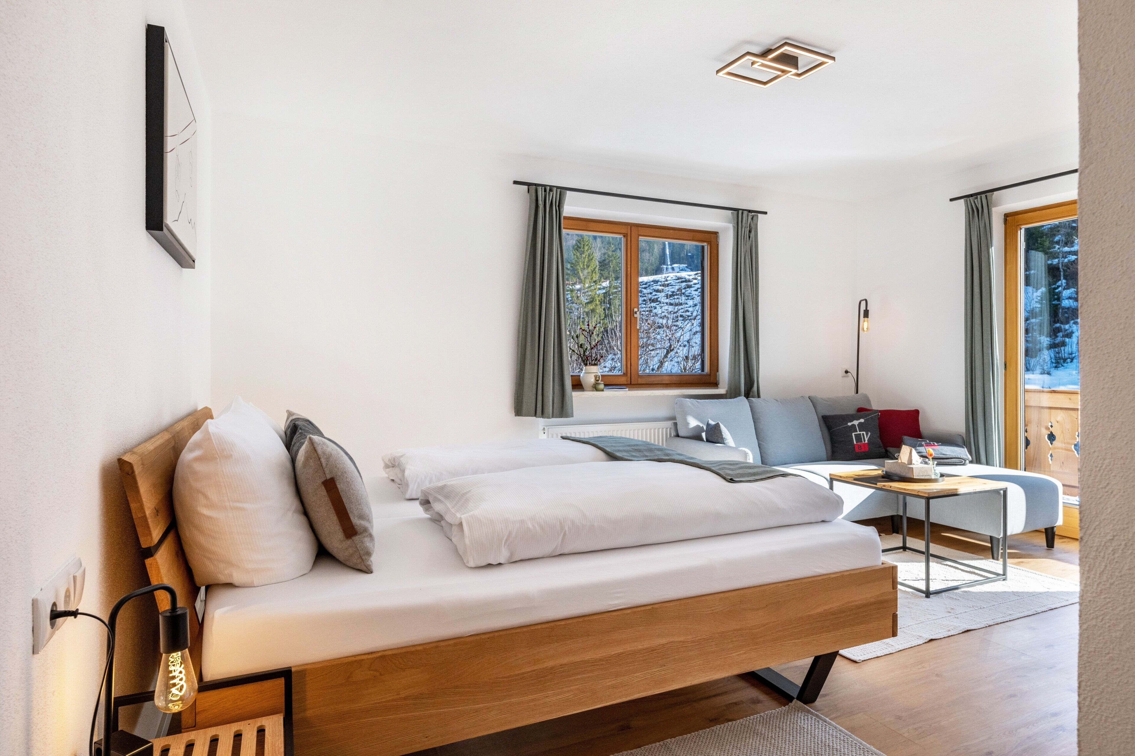 Une chambre moderne avec un lit en bois, une petite table et une vue sur un paysage enneigé par la fenêtre.