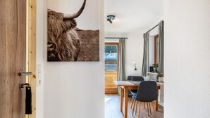 A wooden door with a black handle, a dining area with a table and chairs, and a view of a room with a window and curtains. - Apartment 'Fewo Am Steinbach - Stoaboch' with Mountain View, Balcony and Wi-Fi (Reit im Winkl)