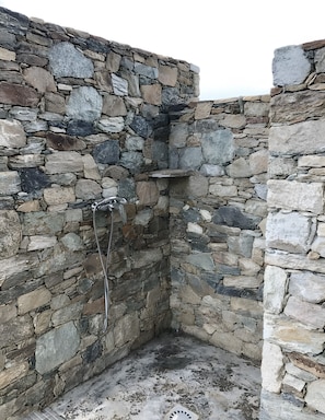 A stone-walled shower enclosure with a metal showerhead and a drain.