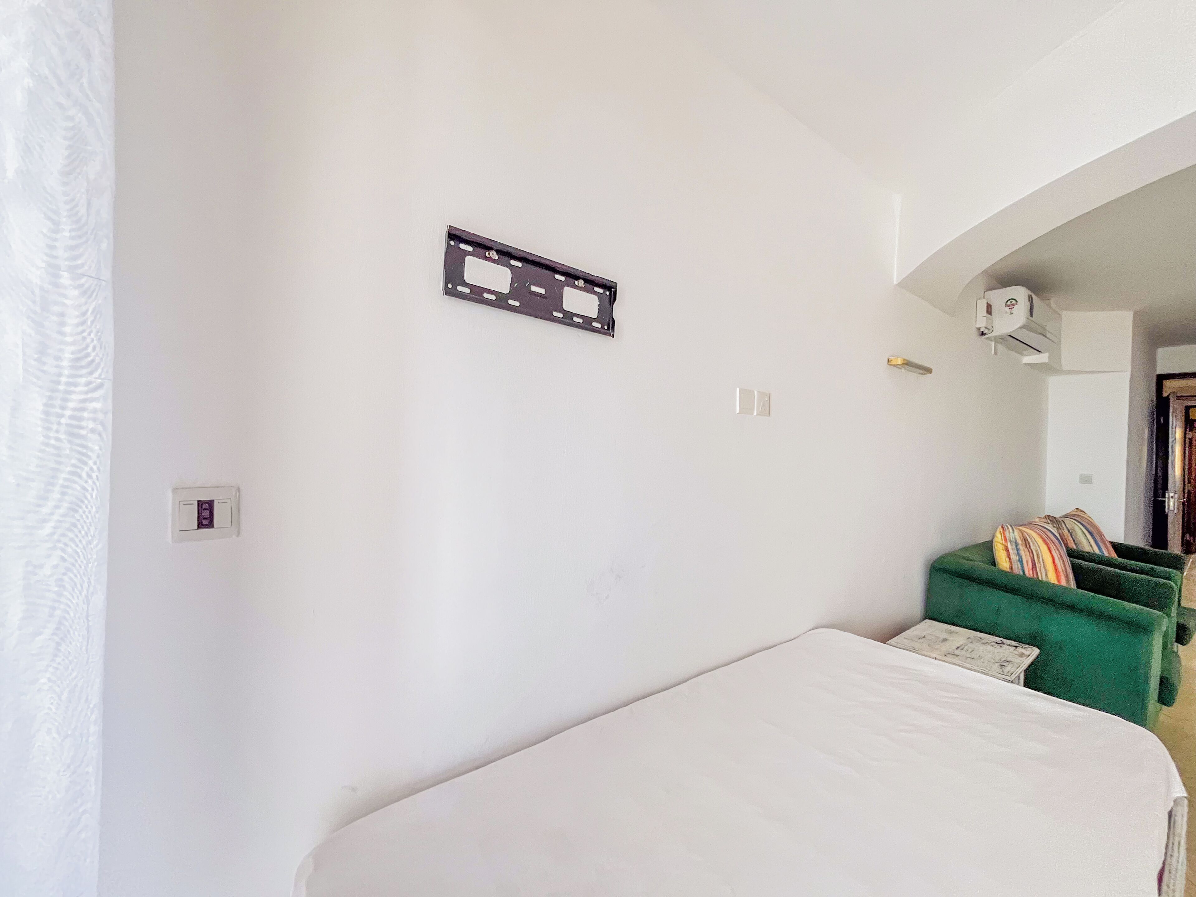 A room with a bed, a green sofa, a wall-mounted air conditioning unit, and a power outlet.
