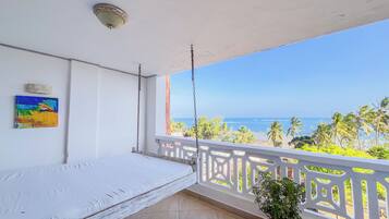 Un balcón con cama, vista a la playa y una planta en maceta.