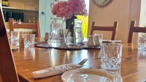 Une table à manger dressée avec des assiettes, des couverts et des verres, ainsi qu’un pichet et des fleurs placés sur la table.