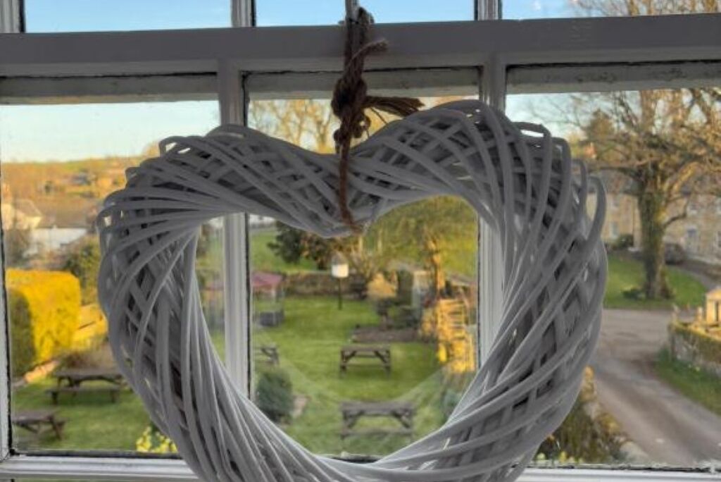 Una decorazione a forma di cuore in vimini bianco appesa a una finestra.