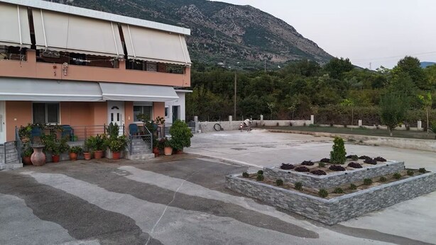 A two-story building with a flat roof, potted plants, and a landscaped area with stone planters.