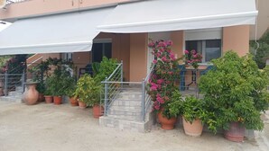 A building with a covered entrance, potted plants, and a staircase leading to the entrance.