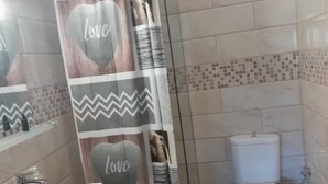 A bathroom with a shower curtain featuring 'Love' and zigzag patterns, a white sink, and a toilet.