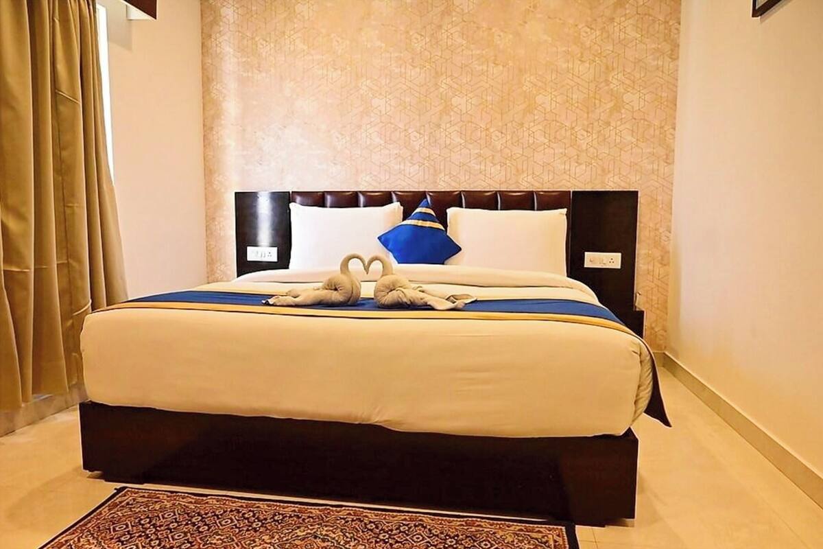 A neatly made bed with a blue and white bedspread, two pillows, and a heart-shaped towel arrangement.
