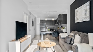 Ein modernes Wohnzimmer mit Fernseher, Sofa, Couchtisch und einer Küche im Hintergrund.