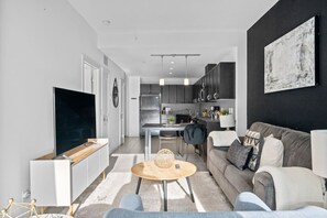 Ein modernes Wohnzimmer mit Fernseher, Sofa, Couchtisch und einer Küche im Hintergrund.