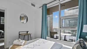Ein Hotelzimmer mit einem Bett, einem Sessel, einem kleinen Tisch, einem Spiegel und einem Fenster mit Vorhängen.