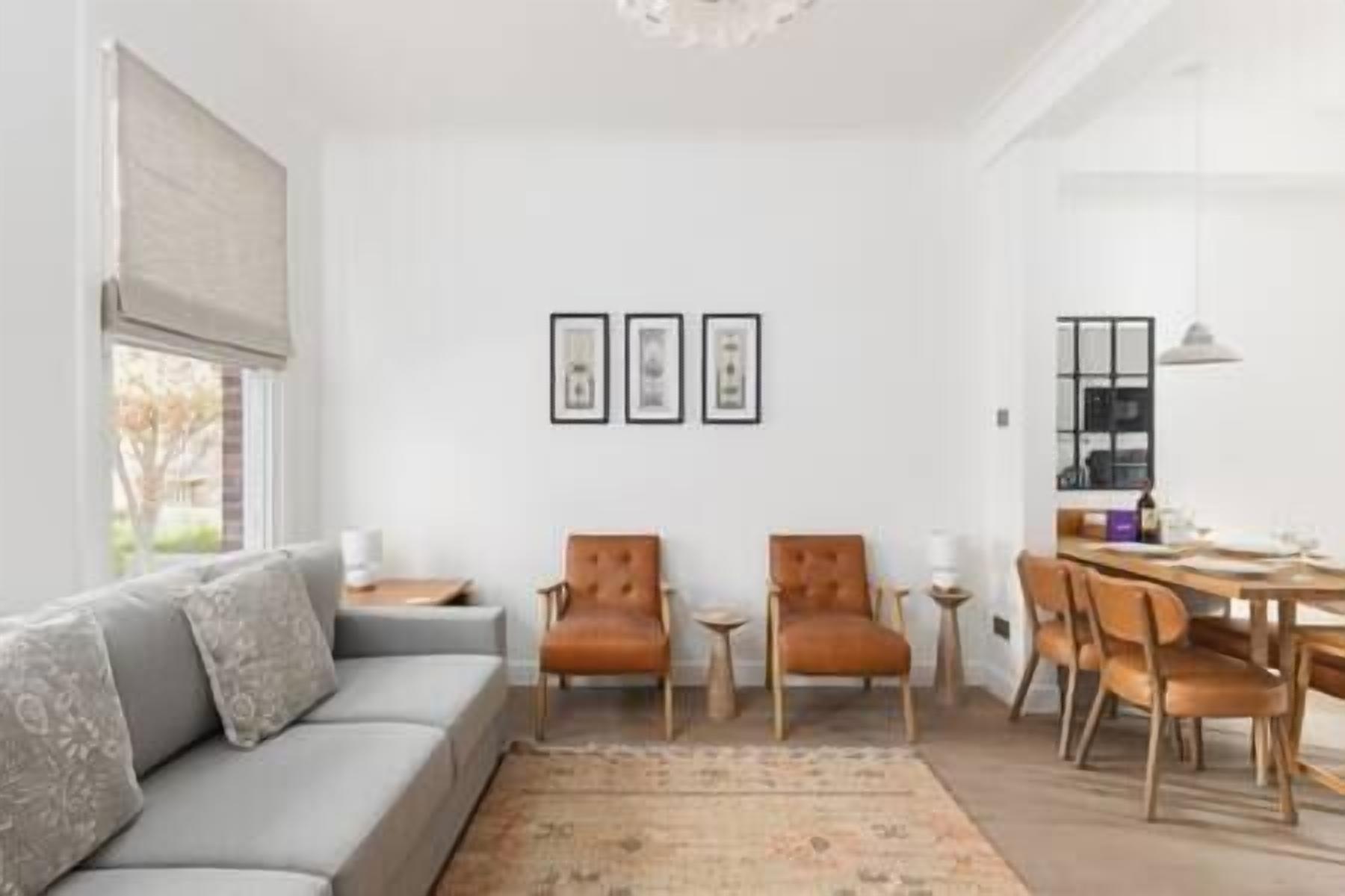 A modern living room with a grey sofa, two leather armchairs, a coffee table, and a dining area with a wooden table and chairs.