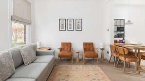 Un salon moderne avec un canapé gris, deux fauteuils en cuir, une table basse et un coin repas comprenant une table et des chaises en bois.
