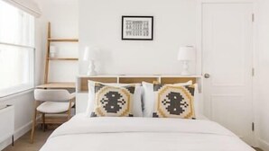 Une chambre d’hôtel avec un lit, une chaise, une table de chevet, une lampe et un tableau encadré au mur.