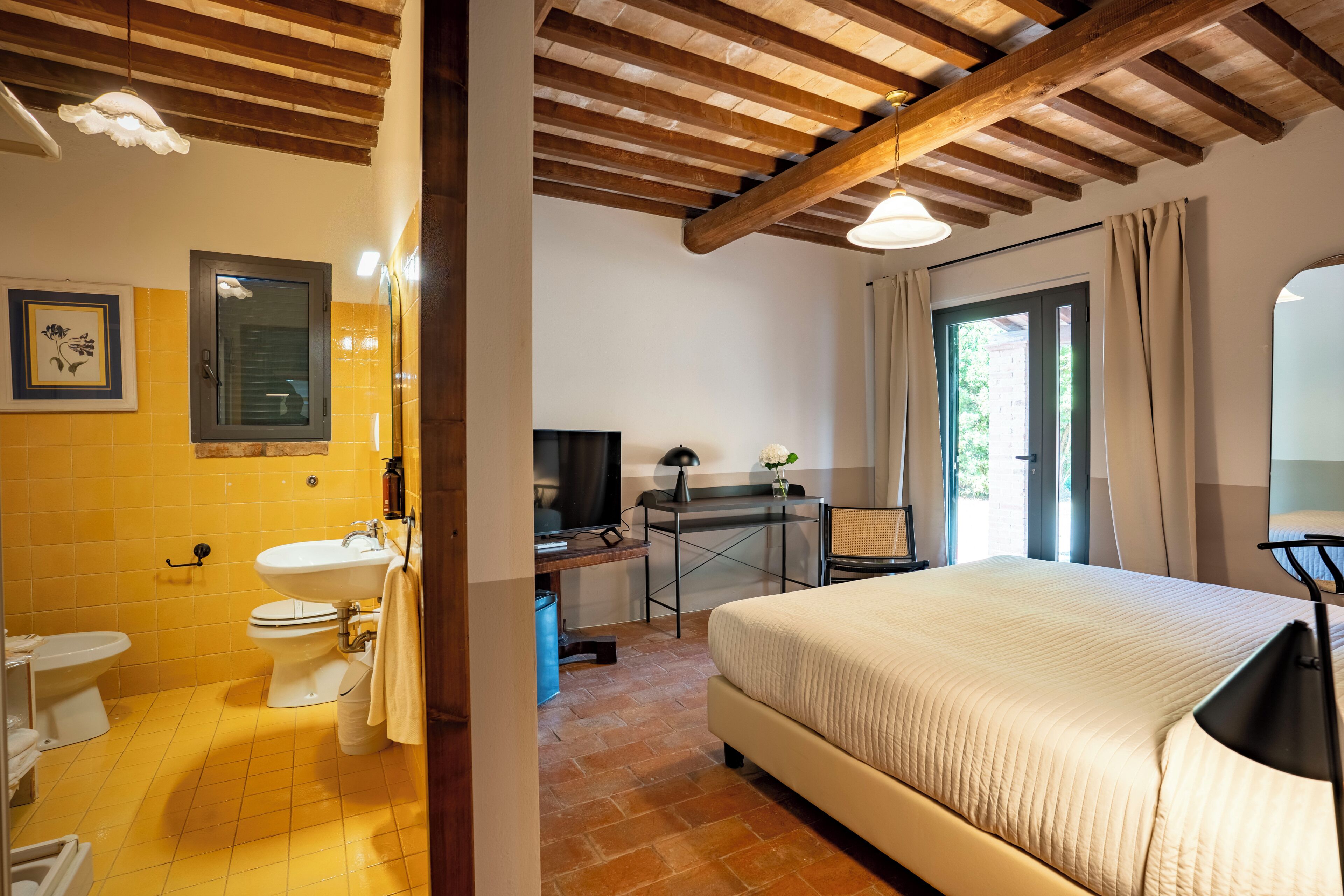 A bedroom with a bed, a desk, a television, and a bathroom with a sink and toilet.