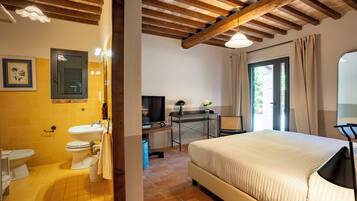 A bedroom with a bed, a desk, a television, and a bathroom with a sink and toilet.