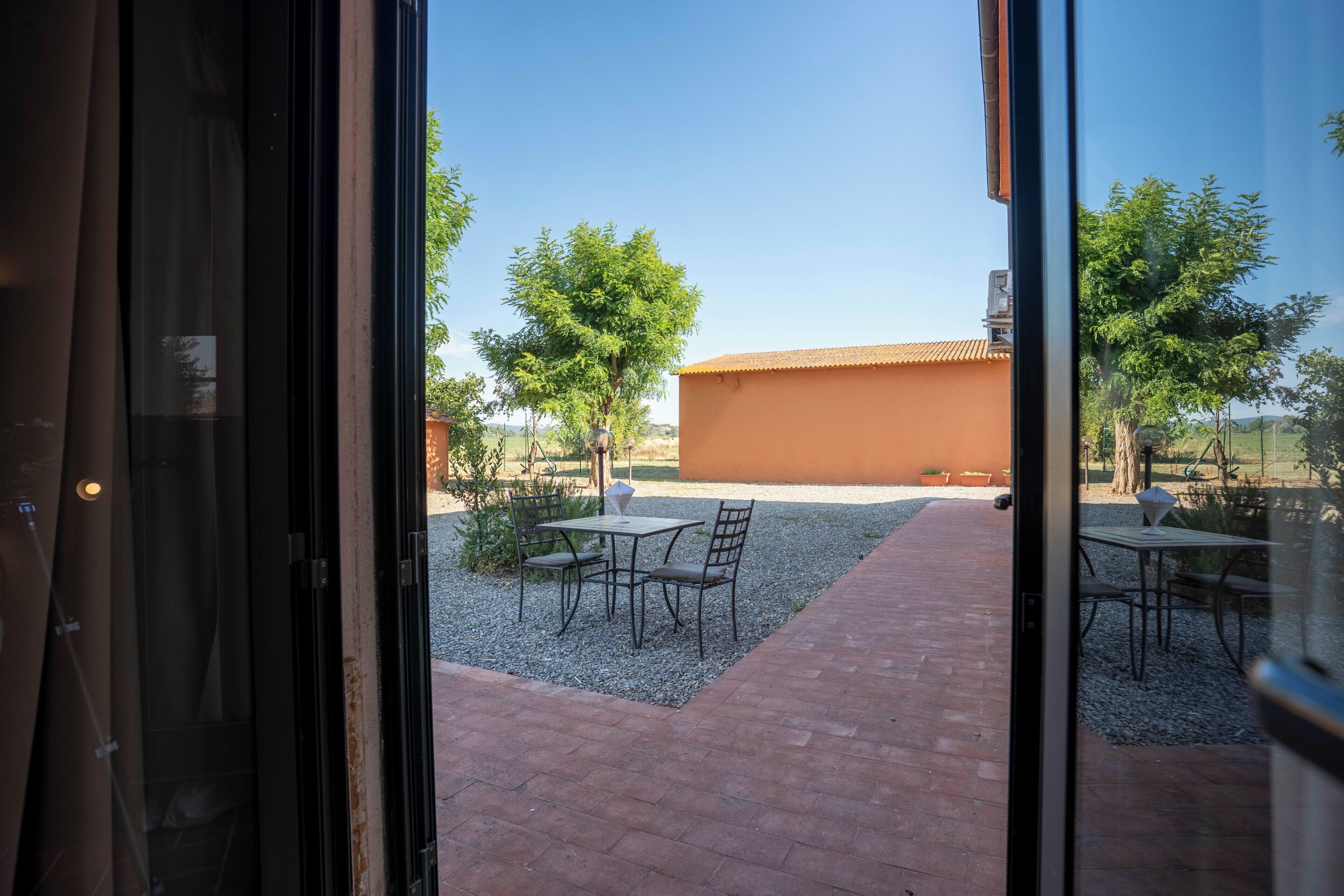 An outdoor patio area with tables and chairs, a gravel path, and a building with a tiled roof.