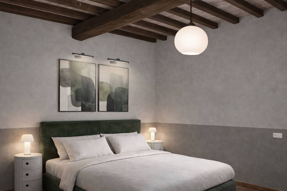 A bedroom with a green upholstered headboard, a bed with white bedding, two bedside tables with lamps, and abstract artwork on the wall.