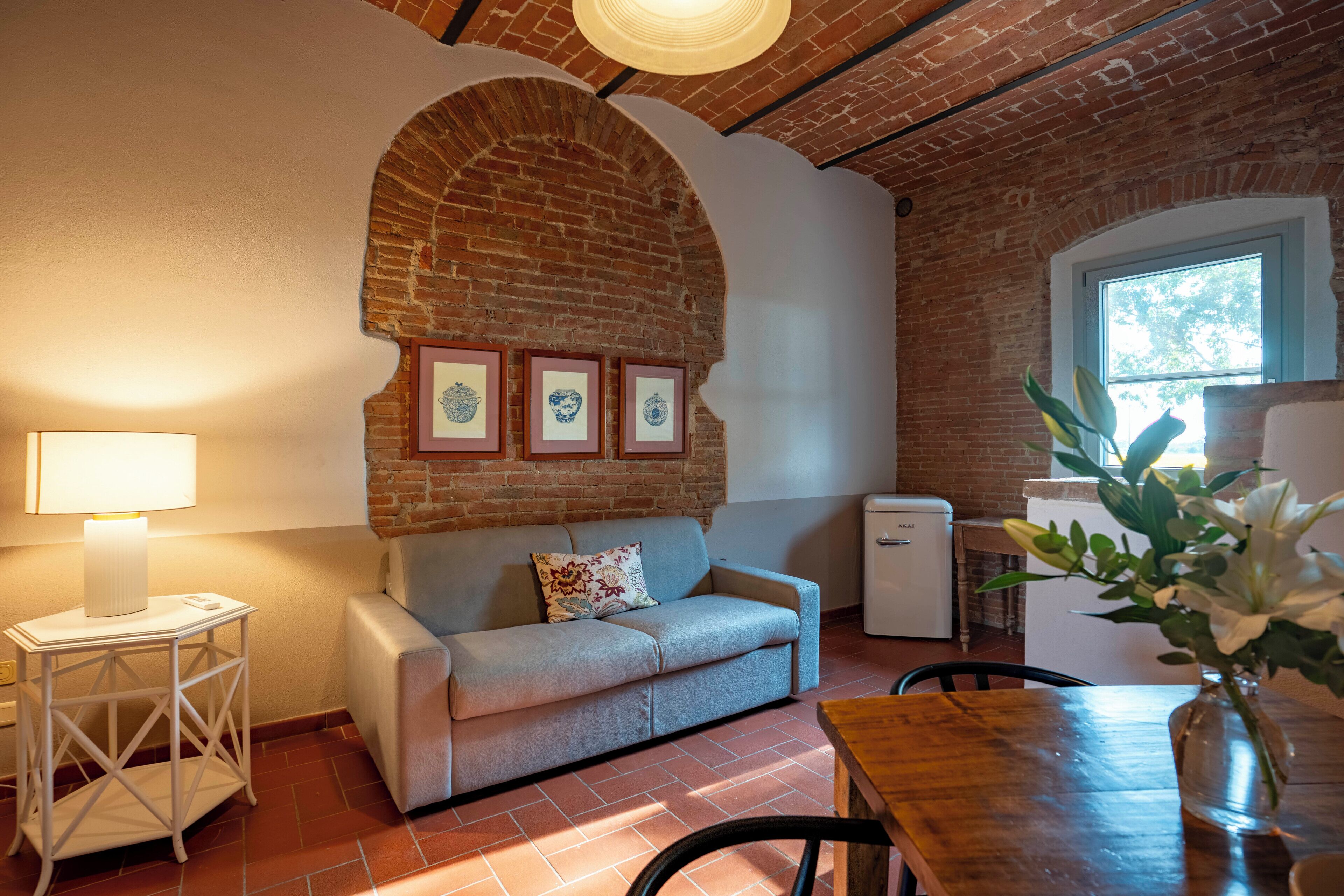 Um quarto aconchegante com parede de tijolos, um sofá, uma mesa pequena e um refrigerador.