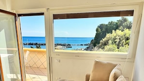 Una sala de estar moderna con un sofá beige y un ventanal con vistas al mar y a la costa rocosa.