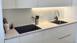 Una cocina moderna con armarios blancos, encimera negra, pileta de acero inoxidable y horno empotrado.