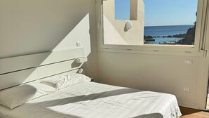Un dormitorio con cama, ventana y vista al mar.