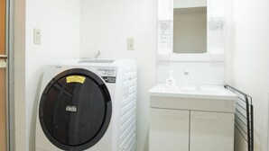 A compact laundry room with a front-loading washing machine, a sink, and a mirror above it. - OPEN Sale! Walking distance from Umeda area / Easy access to Namba and Dotonbori / 10 minutes to USJ by train / Max. 8 people (Kita-ku, Osaka-shi)