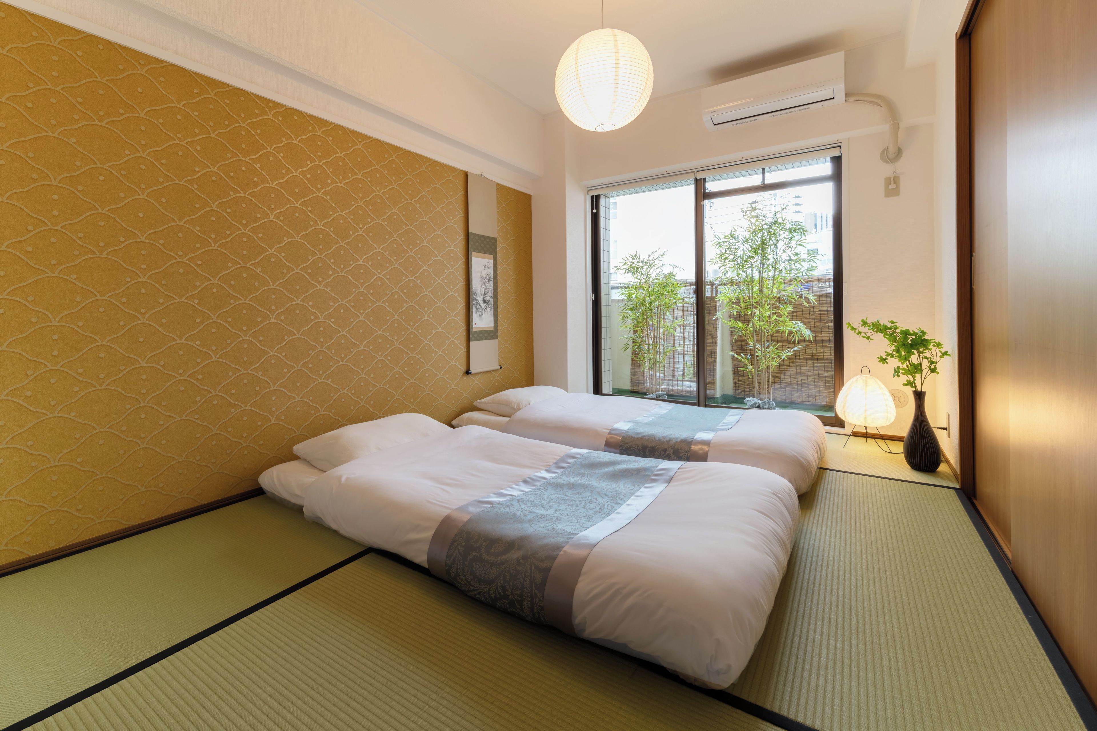 A hotel room with two beds, a large window, and a view of greenery outside.