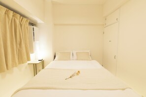 A neatly made bed with a single flower, a bedside table with a lamp, and a wardrobe in a minimalistic room. - OPEN Sale! Walking distance from Umeda area / Easy access to Namba and Dotonbori / 10 minutes to USJ by train / Max. 8 people (Kita-ku, Osaka-shi)