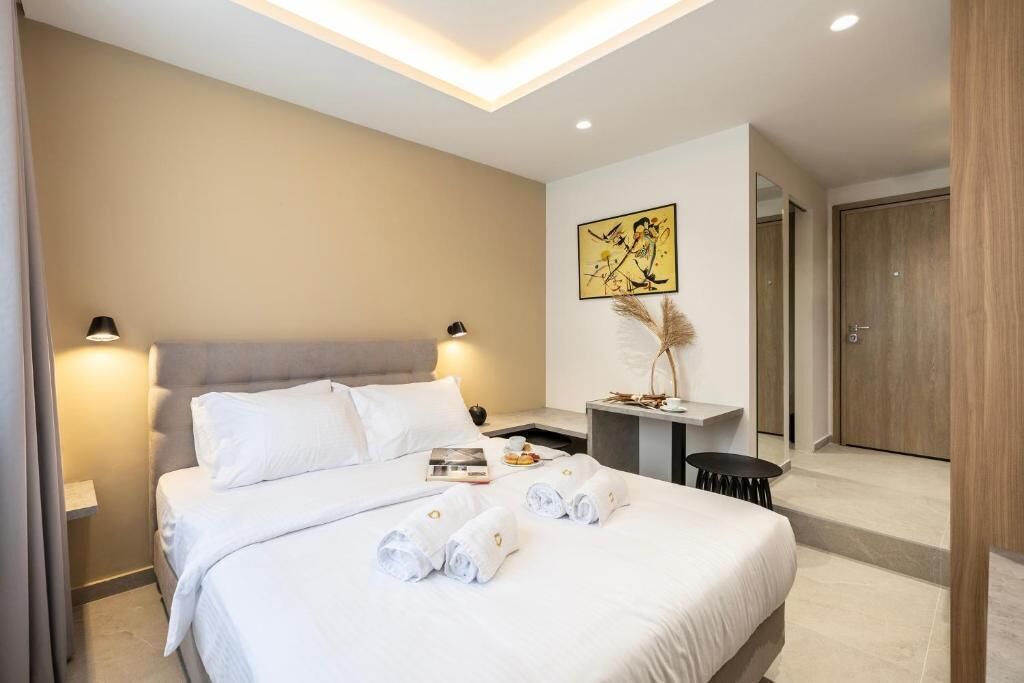 A modern hotel room with a large bed, bedside tables, a small desk, and a door.