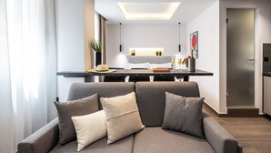 A modern living room with a grey sofa, a dining area with a black table, and a kitchen in the background. - DOMIOS Suites Athens (Athens)