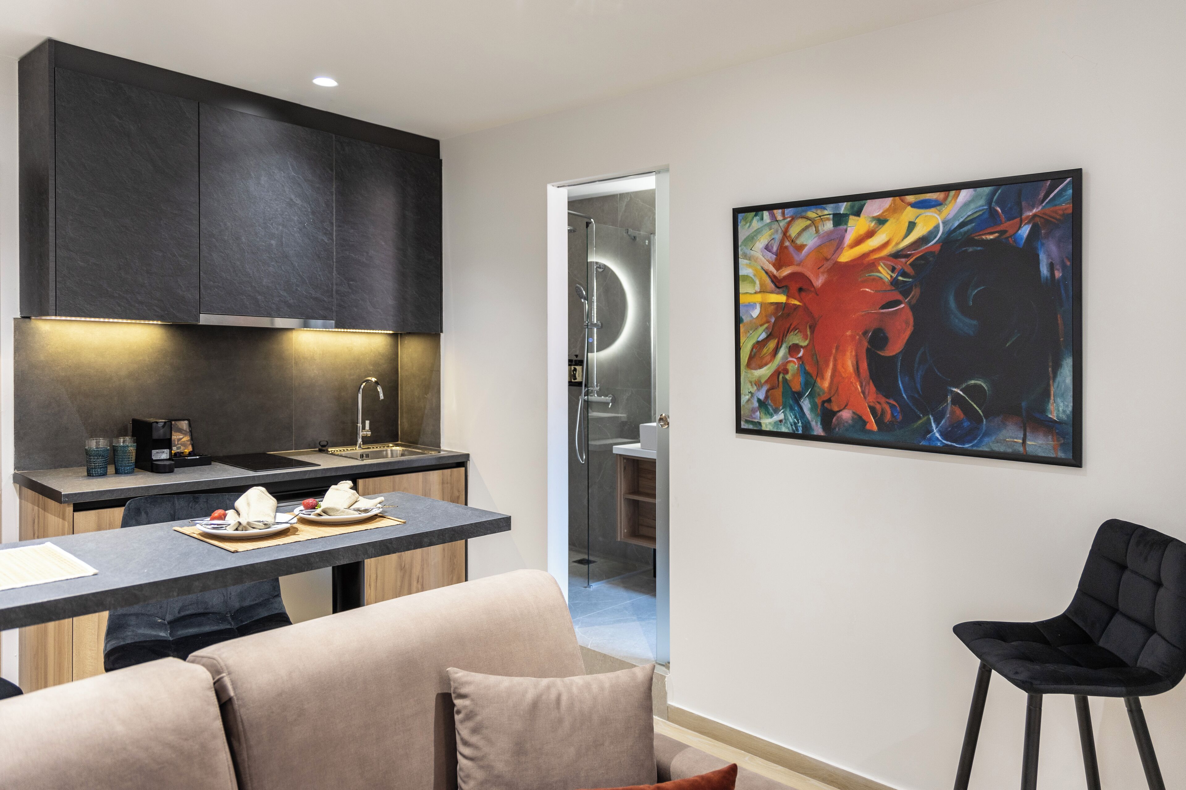 A modern kitchen with dark cabinets, a dining area with a table set for two, and a black chair.